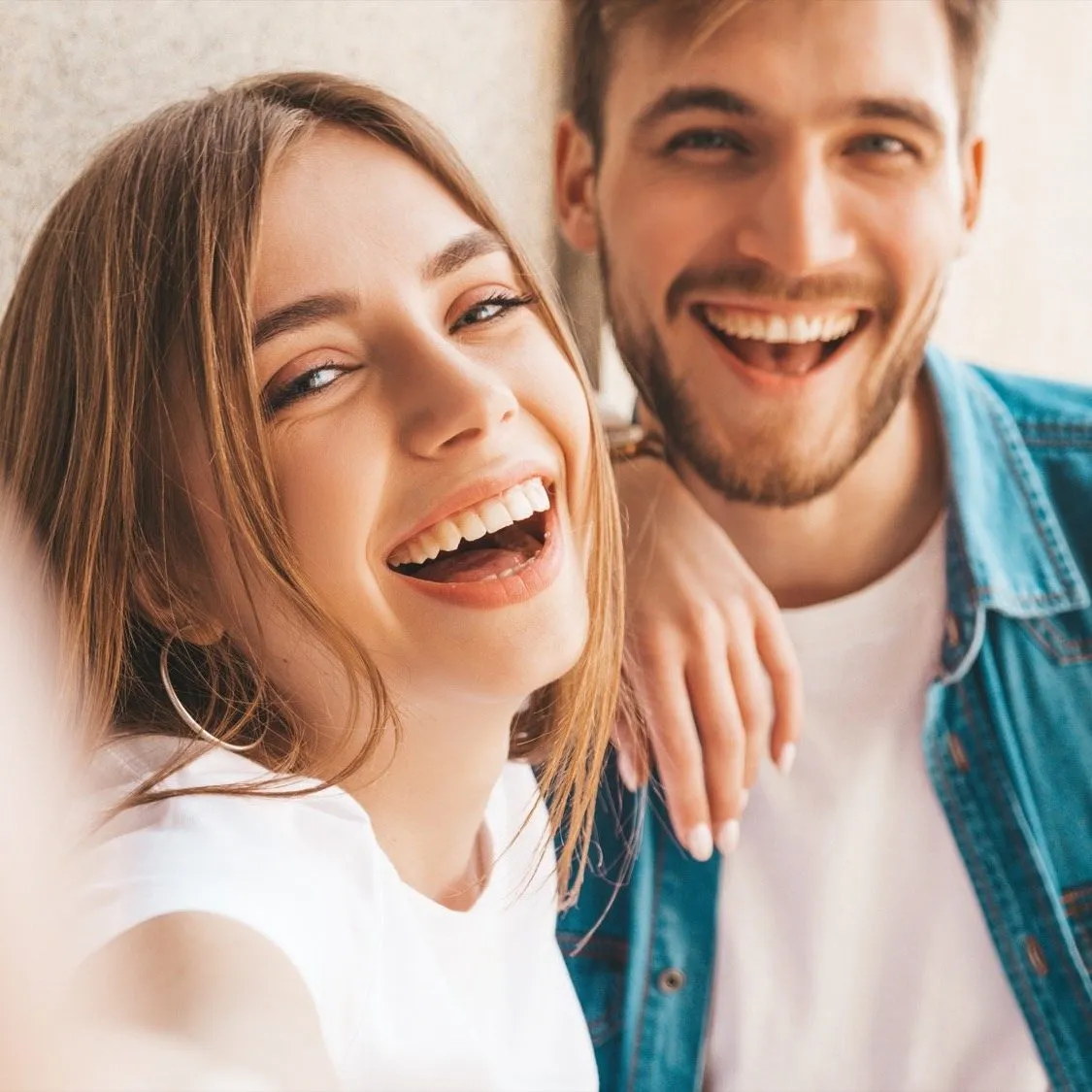 Smiling beautiful girl and her handsome boyfriend in casual summer clothes. Happy family taking selfie self portrait of themselves on smartphone camera. Having fun on the street background Healthy couple paying for dental services