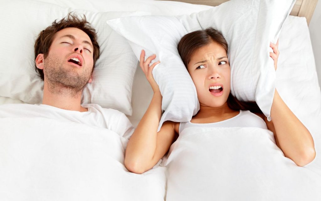 Couple in bed with man snoring and wife annoyed