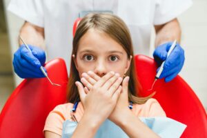 Young girl at the dentist covering her mouth, clearly scared, highlighting dental anxiety treatment at Sierra Smiles Complete Health Dentistry in Reno, NV.