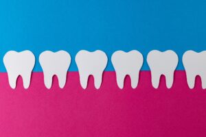 "Paper cutouts of healthy teeth aligned on a pink and blue background, symbolizing gum health and non-surgical periodontal therapy at Sierra Smiles Complete Health Dentistry